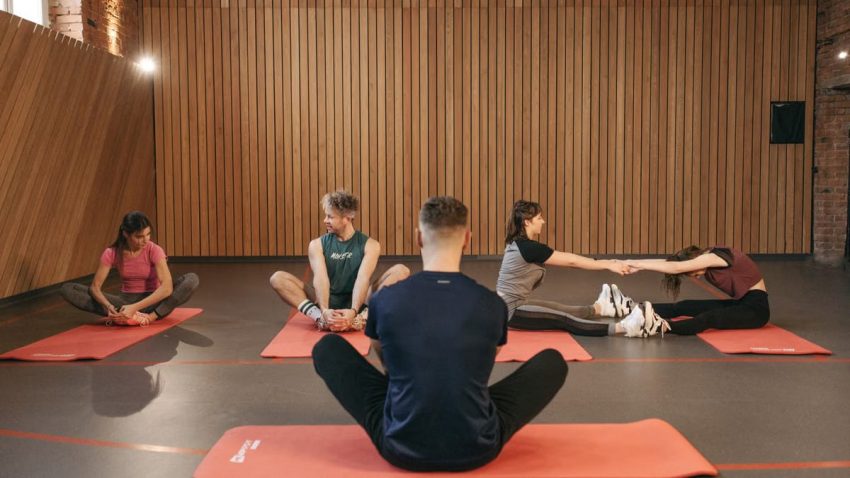 A group of adults practicing yoga and stretching on mats in a wooden panelled room.